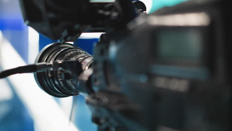 close up camera lens and focus ring with cables reflecting blue studio lights, showcasing intricate optical elements, highlighting precision mechanism and lens coating details broadcast filmmaking