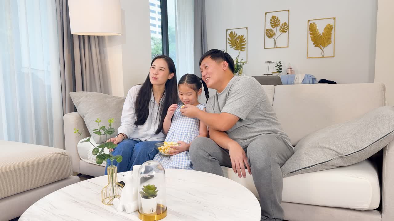 A family of three relaxes together on a cozy sofa in a warmly lit room