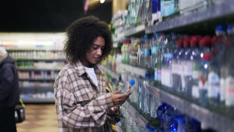 Black-woman-doing-grocery-shopping-in-supermarket,-looking-for-water-bottles