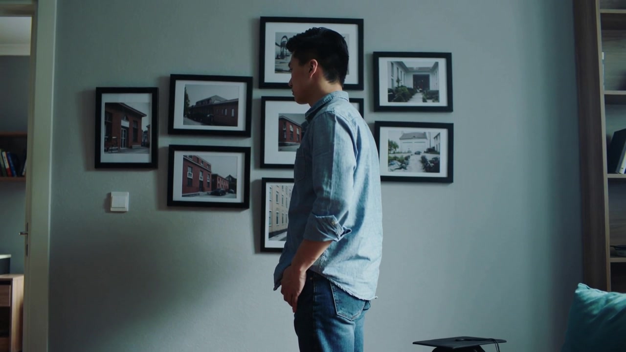 Notando una galleria, un uomo asiatico in camicia abbottonata e jeans che si sposta, studiando quadri a casa con un tocco da laureato.