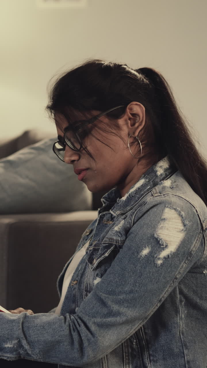 una mujer india lee un libro sentada en una silla de bolsa de frijol mientras una amiga afroamericana estudia en una computadora portátil. los estudiantes se preparan para las clases en la universidad en casa