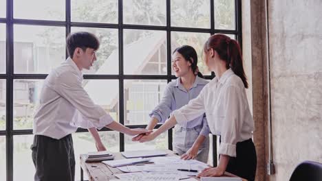 fashionable young asians excitedly stack their hands in smart casual outfits while working in a creative office. the concept was successful.