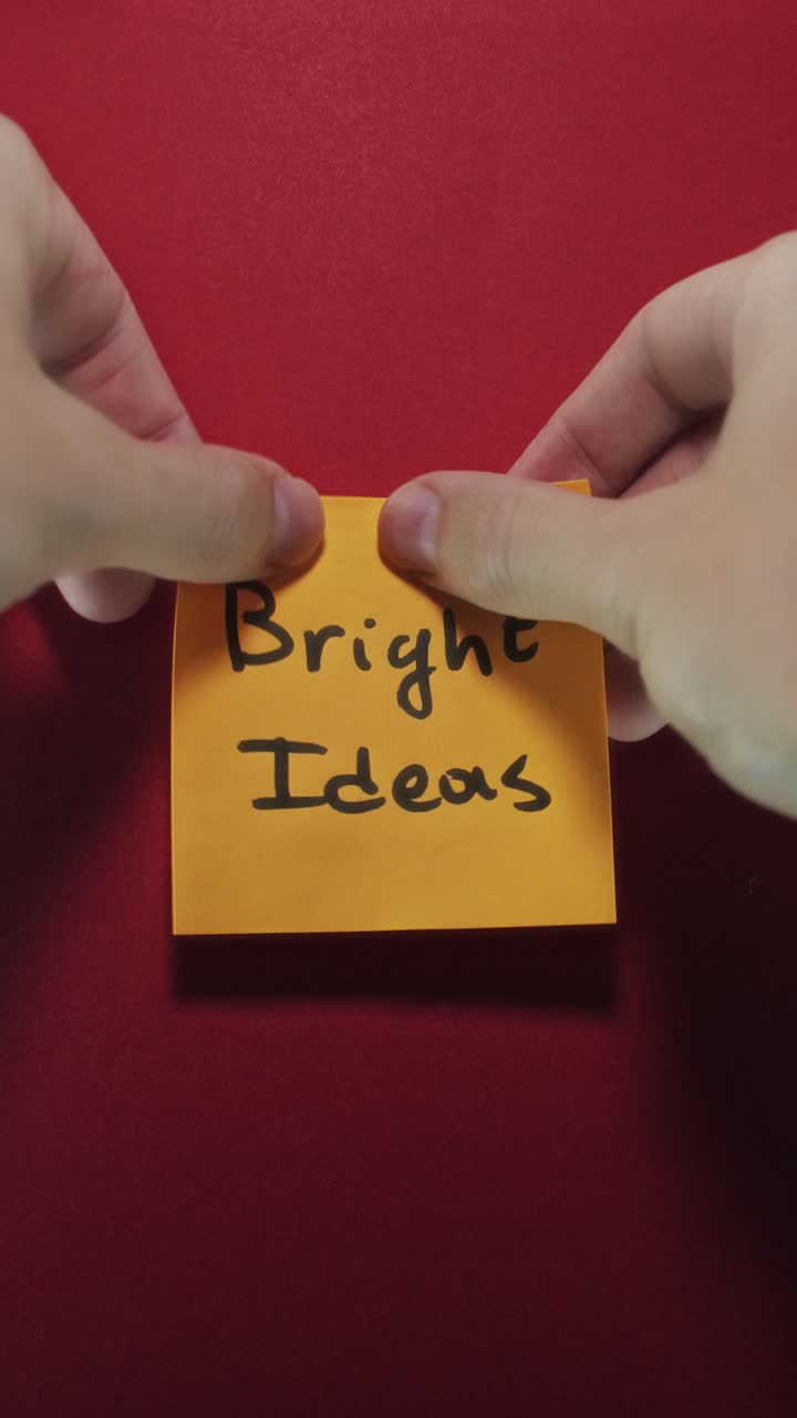 Hands posting Bright Ideas sticky note on red wall, visualizing creativity