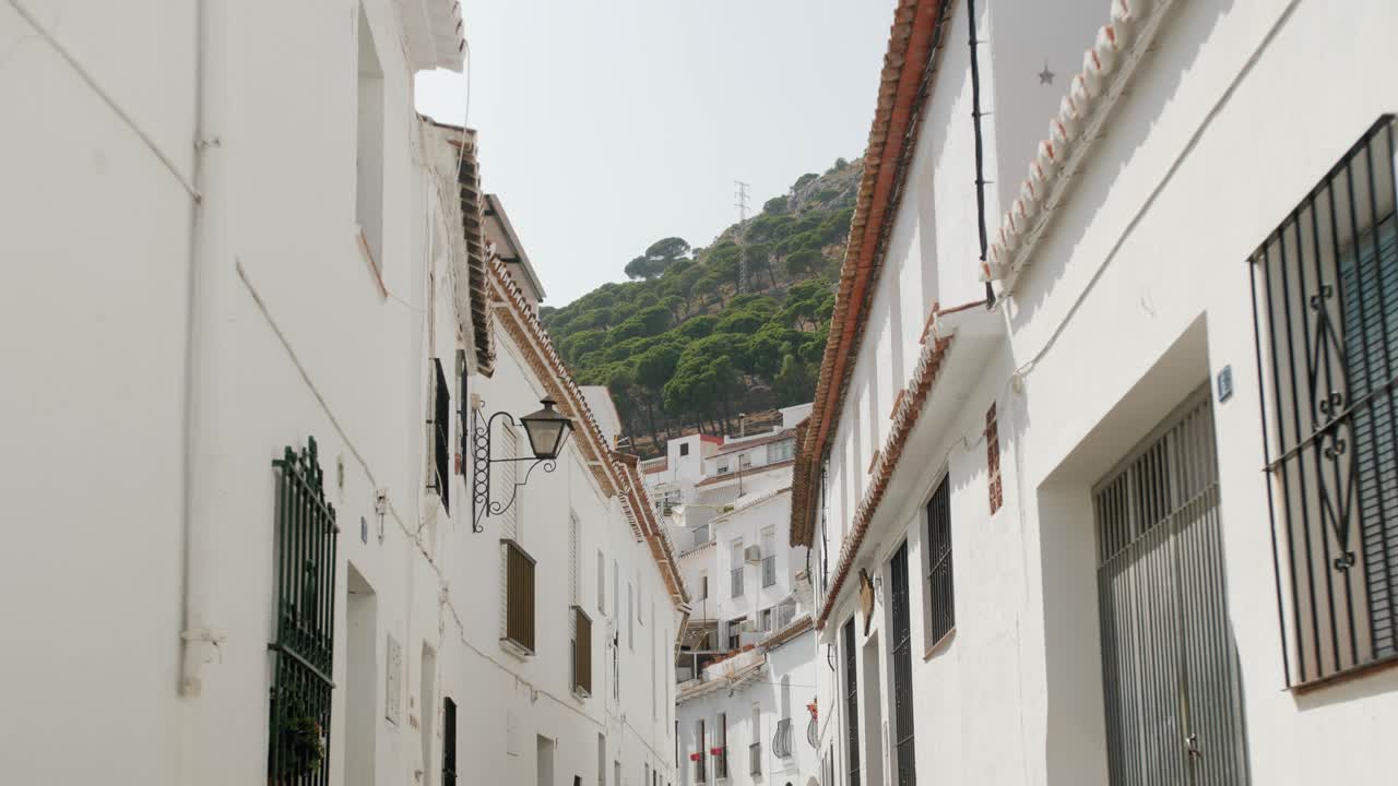 Travelling por uma rua estreita e toda branca de uma vila mediterrânea durante um dia ensolarado.