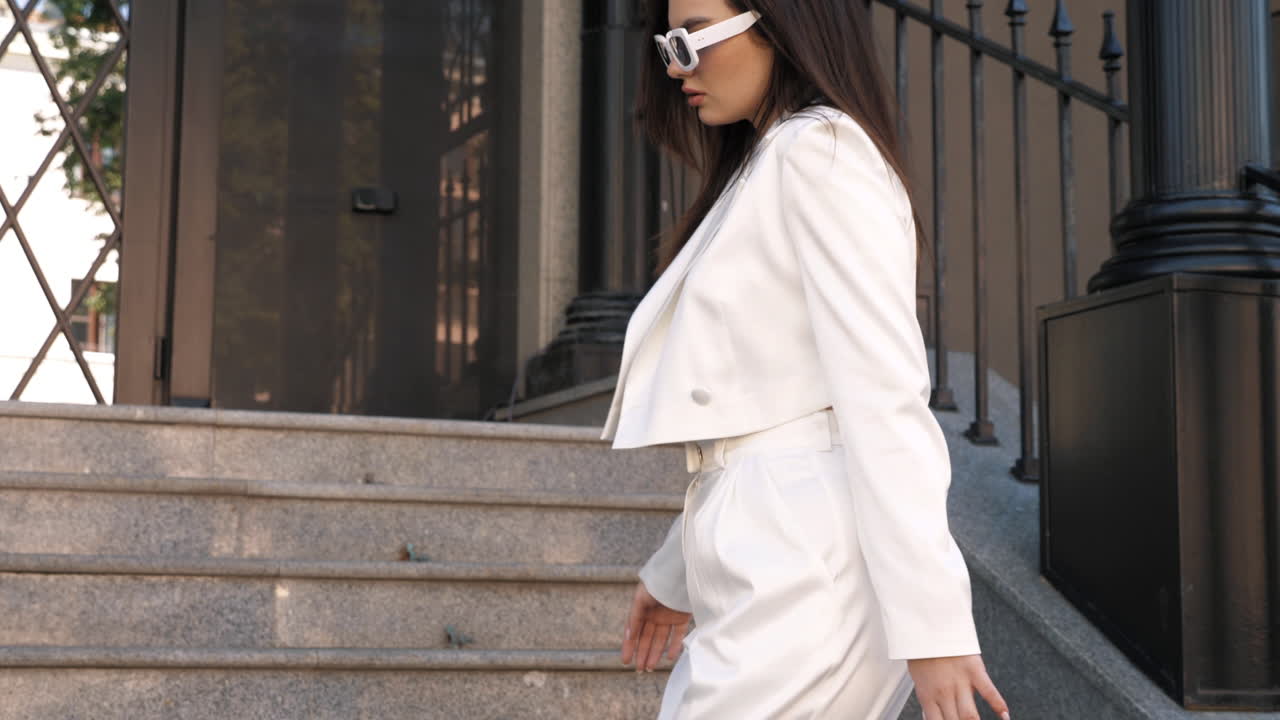 mujer elegante en traje de pantalón blanco en las escaleras de la ciudad