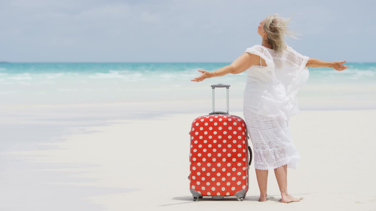 Caucasian senior female on tropical beach with suitcase