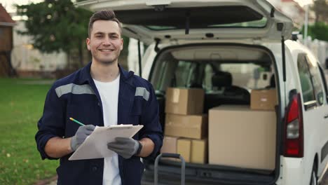 happy smiling delivery service worker makes notes on documents and standing on the street near the minivan. close up footage