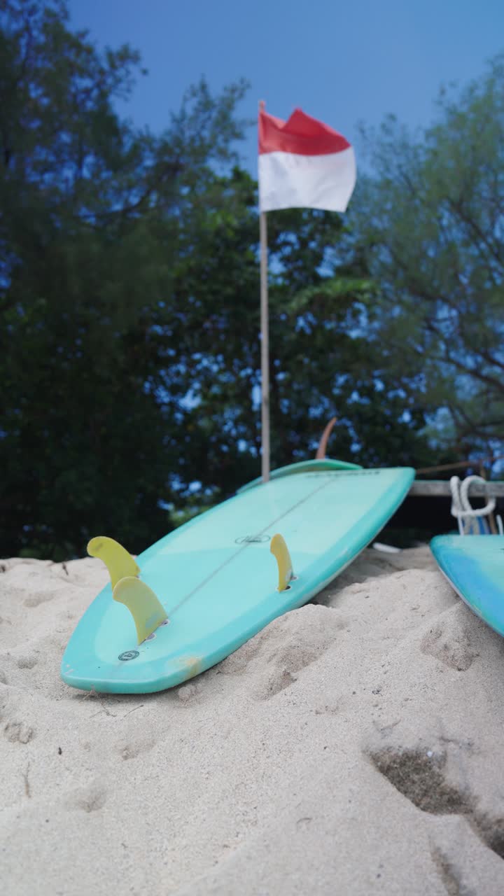 Indonesian flag and colorful sufboards on sandy beach, vertical view