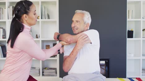 Video-of-happy-biracial-female-physiotherapist-exercising-with-caucasian-senior-man