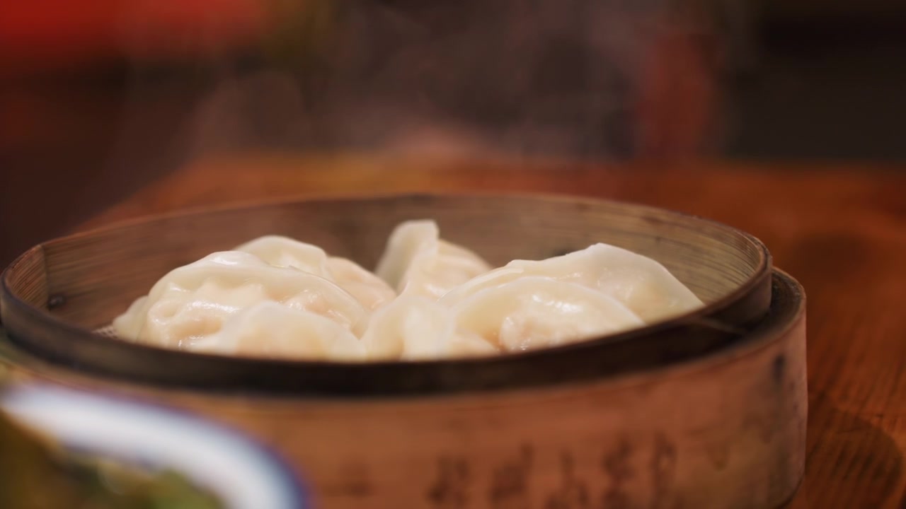 Dimsum kukus dalam kukusan bambu, tampilan dekat di meja kayu. Bokeh restoran hangat, uap mengepul, lipatan buatan tangan, adonan lembut, isian mengkilap. Sajian koki yang menciptakan suasana nyaman dan membangkitkan selera.