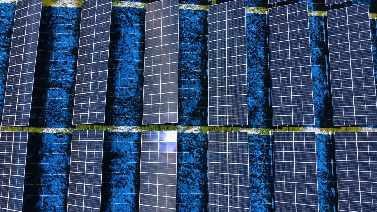 Vista dall'alto simmetrica di pannelli solari con riflesso. Ripresa aerea dall'alto di un impianto fotovoltaico che mostra file simmetriche e un intenso riflesso del sole sul pannello centrale.