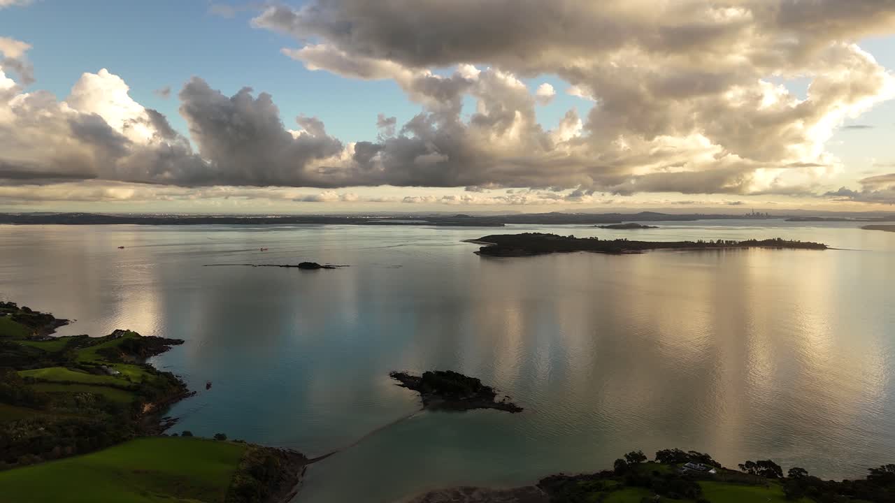 Waiheke Island shore with clouds reflecting in the calm ocean water at sunset