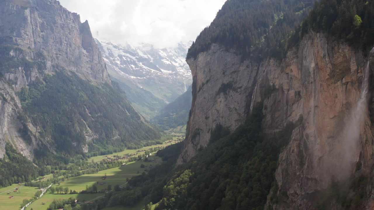 Aerial dolly of waterfall on mountainside to beautiful green valley