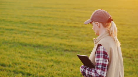 a young woman farmer walks along a wheat field carrying a tablet