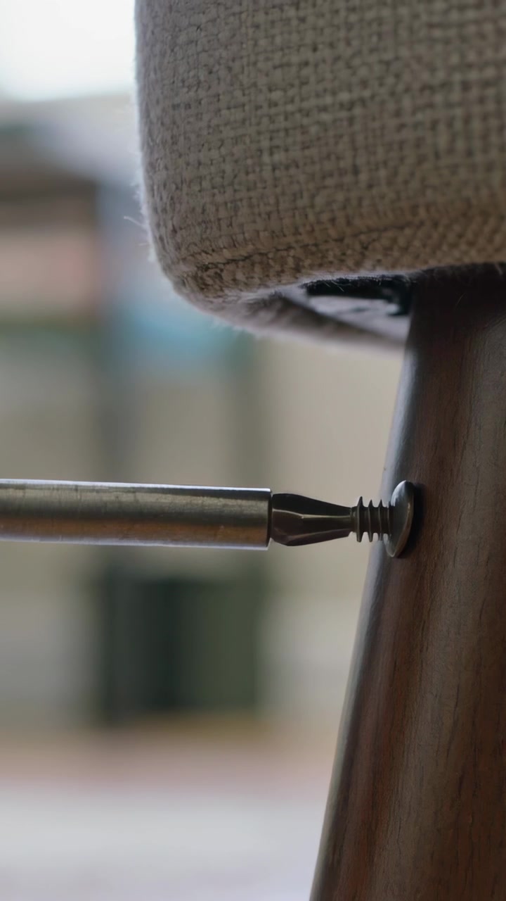 Vertical video: Aligning driver bit, hand rotating and driving screw into leg at home to fix seat
