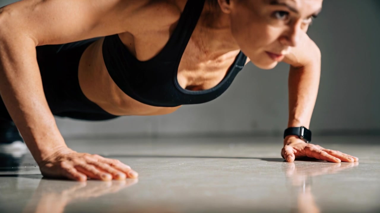 Starting training, woman lowering, pressing up on studio floor, in black sportswear with smartwatch