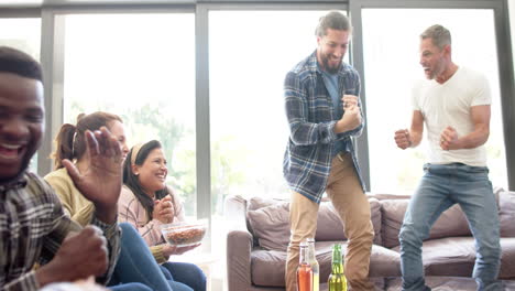 Happy-diverse-male-and-female-friends-watching-sport-on-tv-and-celebrating-victory