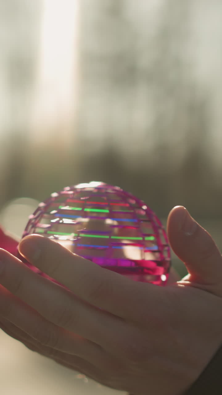 un primer plano de un adulto sosteniendo un pequeño objeto giratorio colorido en sus manos, equilibrándolo cuidadosamente antes de dejarlo caer al suelo