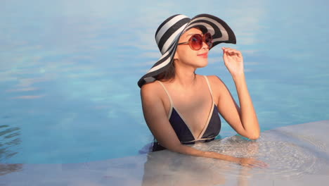 Una-Mujer-Joven-Y-Bonita-Se-Para-En-La-Parte-Menos-Profunda-De-La-Piscina-De-Un-Resort-Ajusta-Sus-Gafas-De-Sol-Mientras-Mira-A-Su-Alrededor