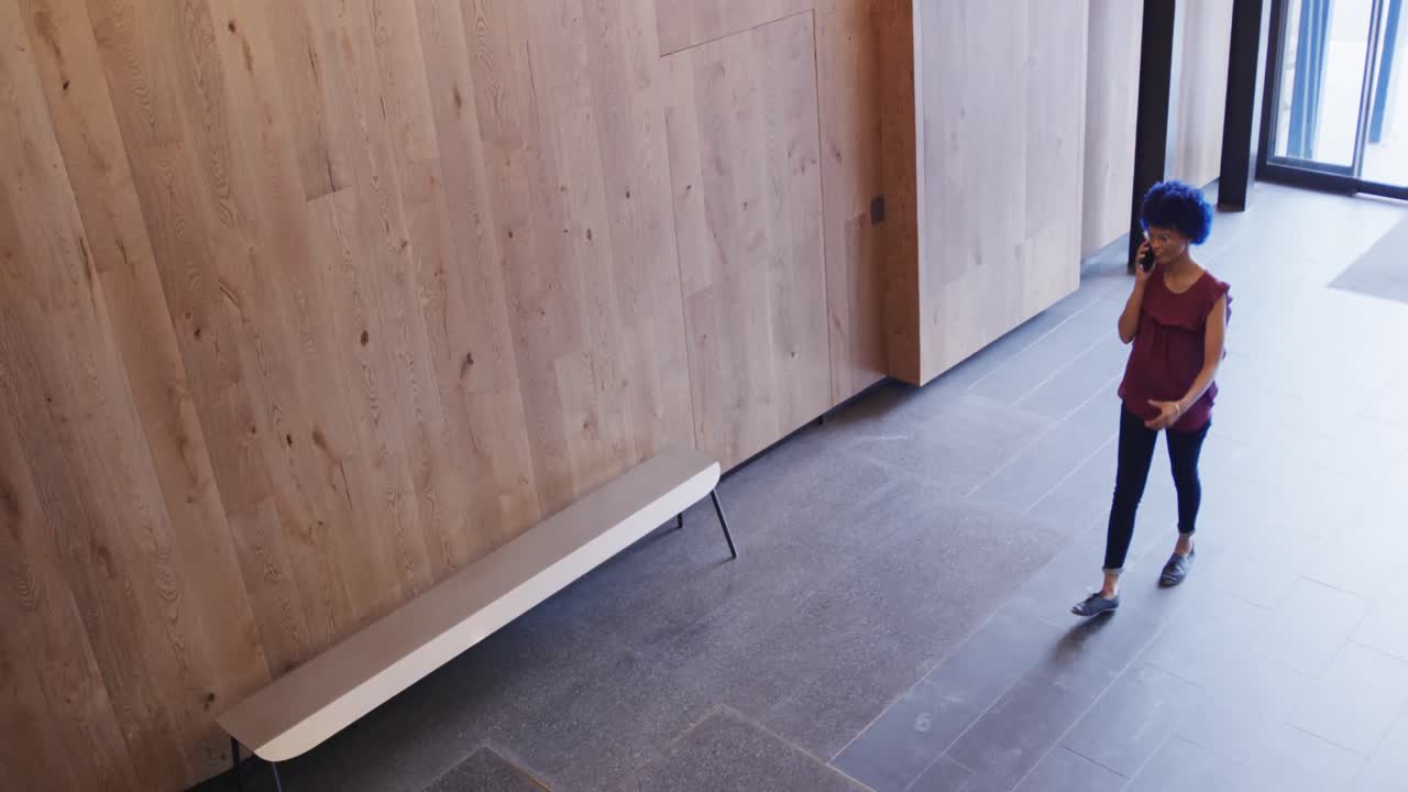 mujer de negocios biracial con afro azul hablando en teléfono inteligente en la oficina, cámara lenta