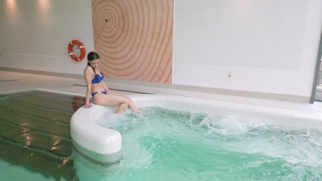 woman sits on jacuzzi edge to test bubbling water with feet in wellness spa