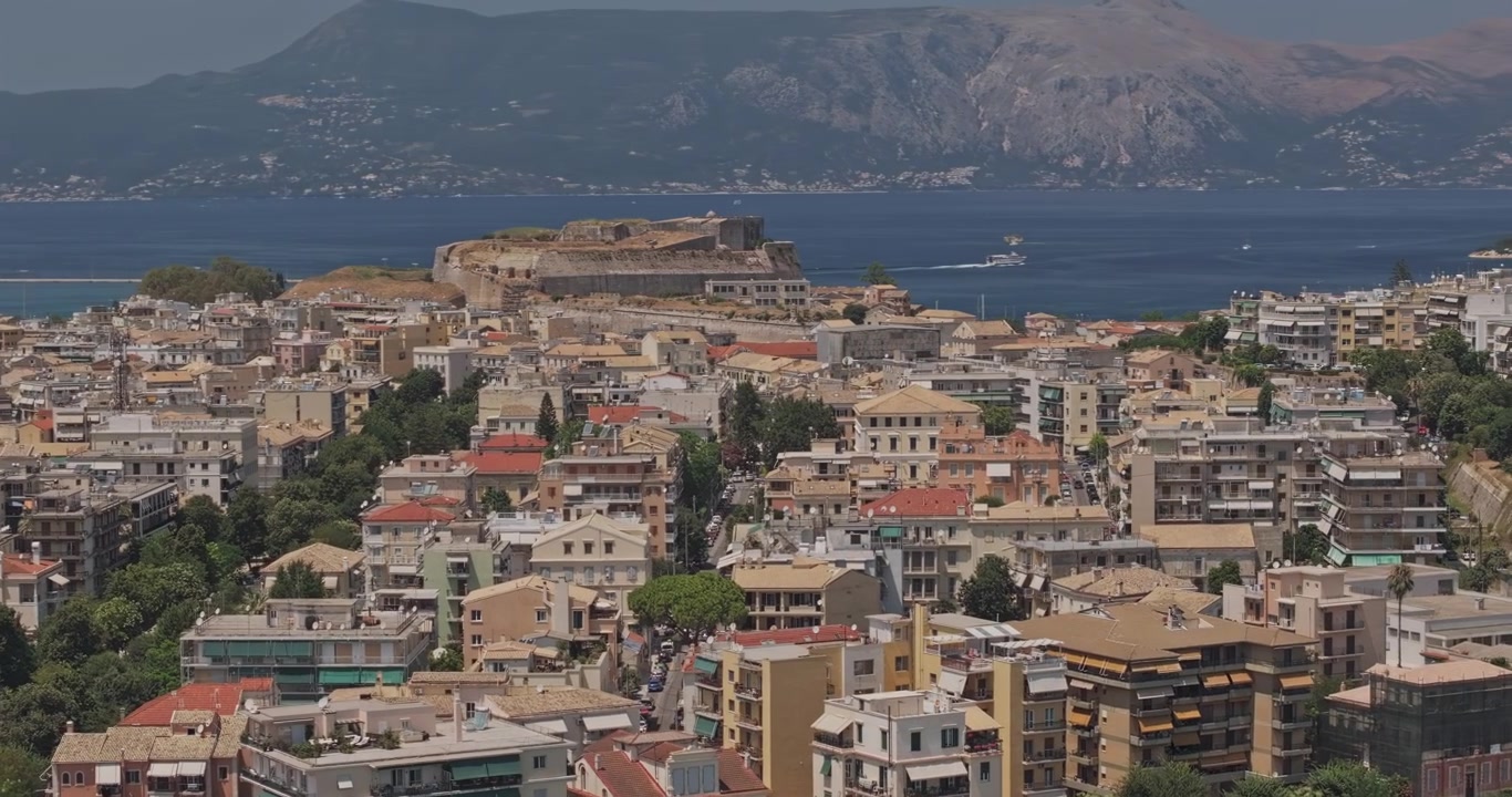 Corfù, Grecia. Sorvolo a bassa quota con teleobiettivo aereo v10 lungo la Baia di Garitsa, che rivela residenze sul lungomare, il centro di Corfù città e le colline dell'isola - Ripreso con Mavic 3 Pro Cine - 16 luglio 2024