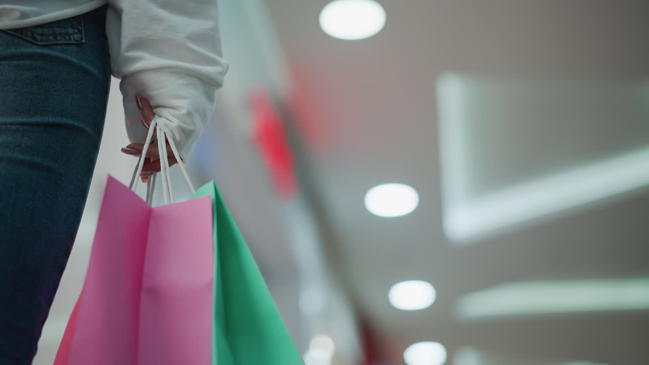 현대 쇼핑몰에서 걸어다니는 여성이 들고 있는 초록색과 분홍색 쇼핑 가방의 클로즈업