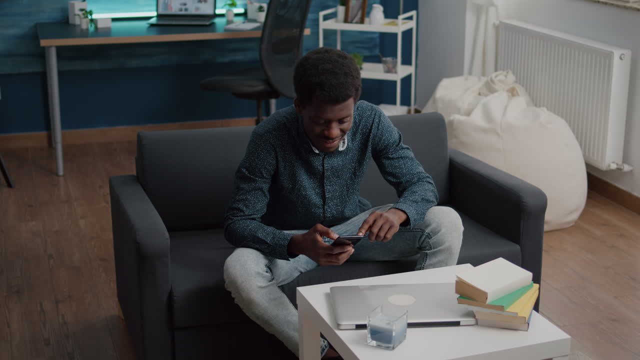 Black guy in his living room using phone to browse social media