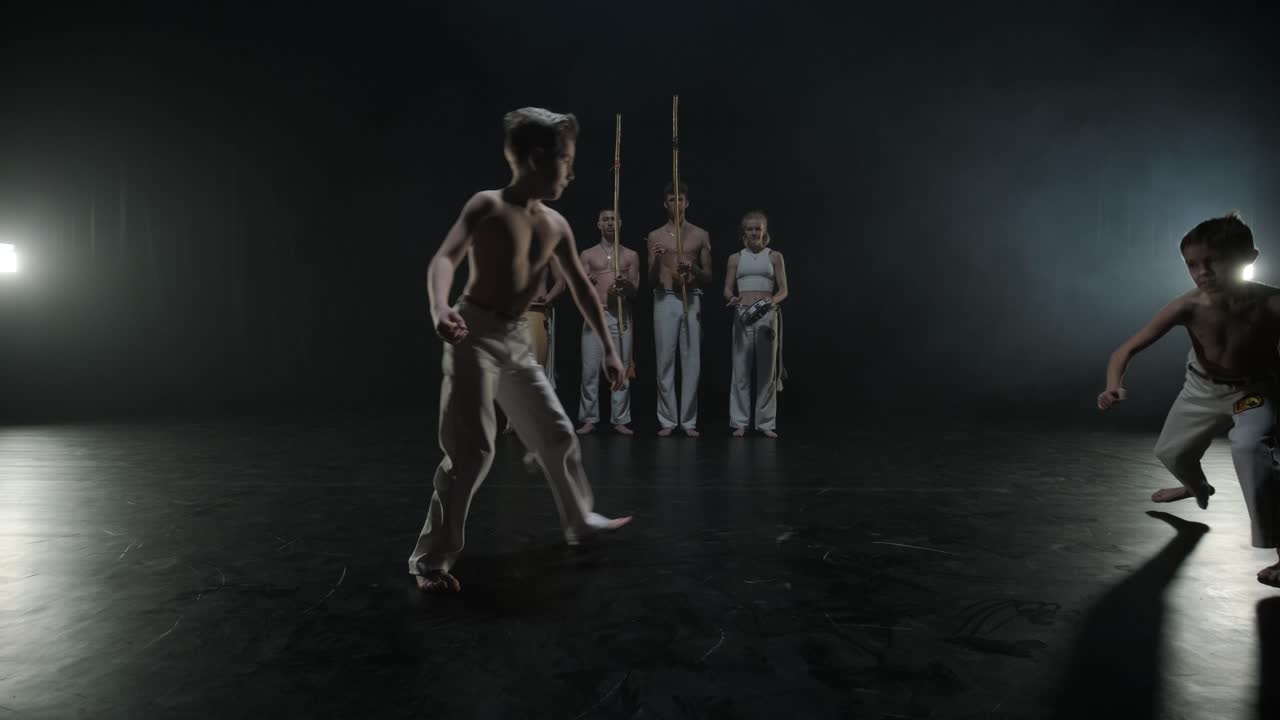 Grupo de dançarinos profissionais praticando capoeira na escuridão contra um holofote em um estúdio com fundo preto. Arte marcial afro-brasileira que combina elementos de dança