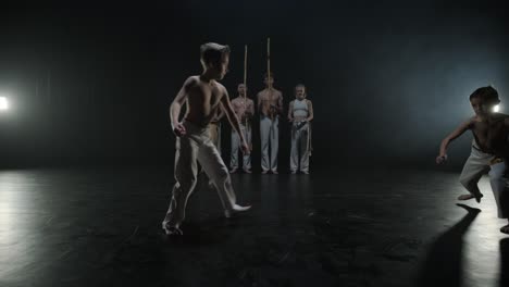 group of a professional dancers are practicing capoeira in darkness against a spotlight on a black background of studio. afro-brazilian martial art that combine elements of dance.