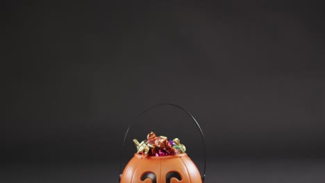 Scary-halloween-pumpkin-printed-bucket-full-of-candies-against-grey-background