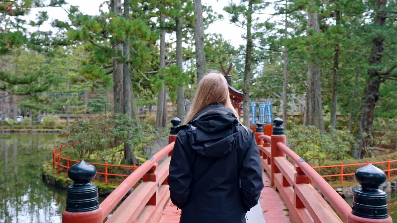 A cinematic scene capturing a blonde girl walking gracefully across a traditional bridge within the sacred grounds of Danjo Garan in Mount Koya, Koyasan, Japan.