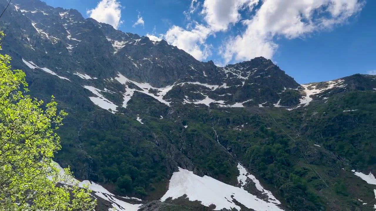 Pomalý panoramatický záběr odhaluje zasněžené horské štíty za zářivě zelenými jarními stromy a listím.