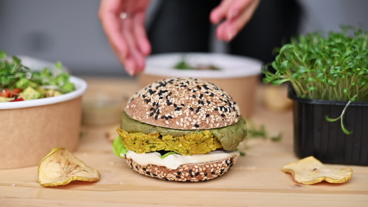 Observa cómo se monta con destreza una colorida hamburguesa vegetal con verduras frescas, untables y una sabrosa hamburguesa. Disfruta de los vibrantes colores y los ingredientes saludables en esta deliciosa preparación de comida.