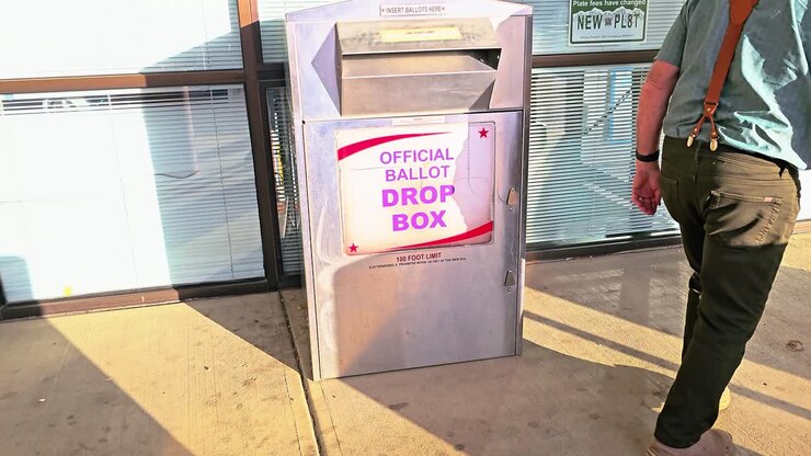 Uomo anziano deposita la scheda elettorale via posta in una cassetta di votazione ufficiale con relativo cartello per le elezioni democratiche americane