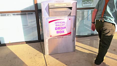 old man drops mail-in ballot letter in slot at official voting box with official ballot drop box sign for american democratic election