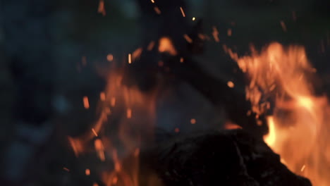 Man-moving-wood-lock-at-Bonfire-close-up-sparks-outdoor-wilderness-close-up-slow-motion