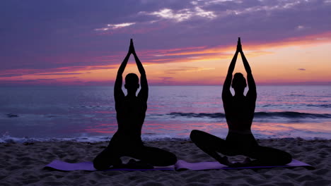 couple practicing yoga at sunset beach