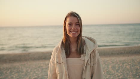 Portrait-of-a-young-beautiful-blonde-girl-who-looks-at-the-camera-and-smiles-against-the-backdrop-of-the-sea-in-the-morning