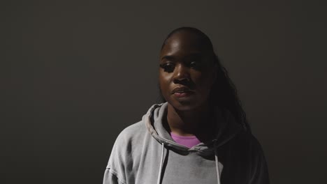 cabeza y hombros retrato de estudio de una mujer joven con capucha con iluminación baja contra un fondo gris