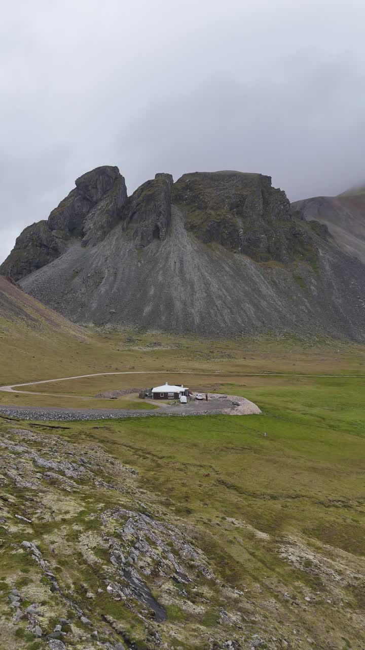 A single home near the base of the famous Vestrahorn mountain in Iceland, vertical drone footage.