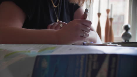 a traveler's focused hands holding a pen over a spread-out city map, with a smartphone and notes on the side