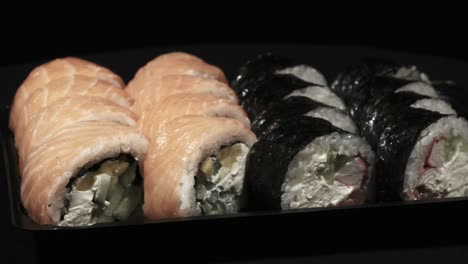los rollos de sushi giran en un recipiente de plástico sobre un fondo negro. entrega de comidas