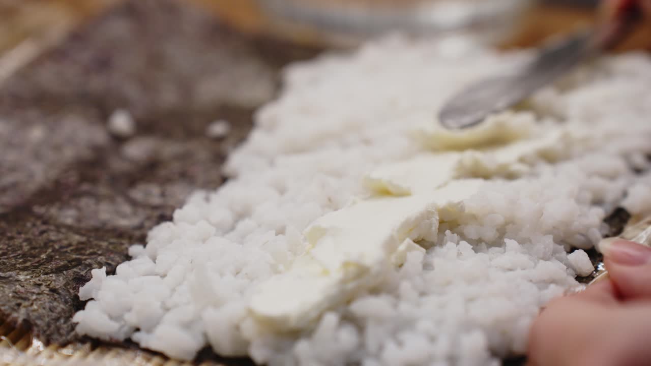 detalle de primer plano de cuchillo untando queso encima de arroz, rollo de sushi