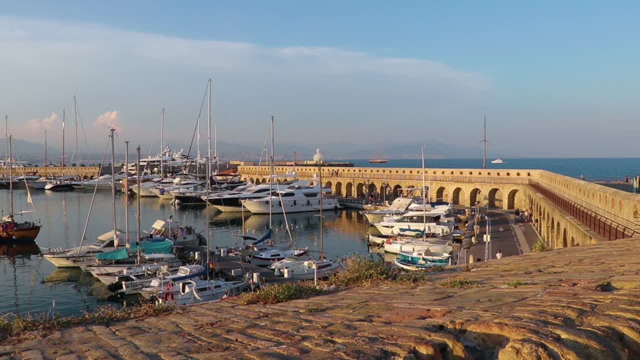 Boats in Port Vauban in Antibes, southern France. Statue "Le Nomade" by Jaume Plensa showing by the horizon. Establishing shot.