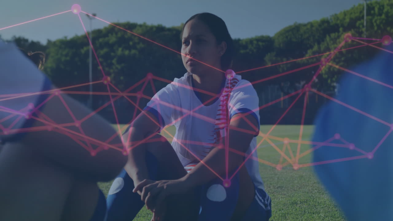 Female soccer player kneeling hugging knees on grass field, showing sports tech network overlay
