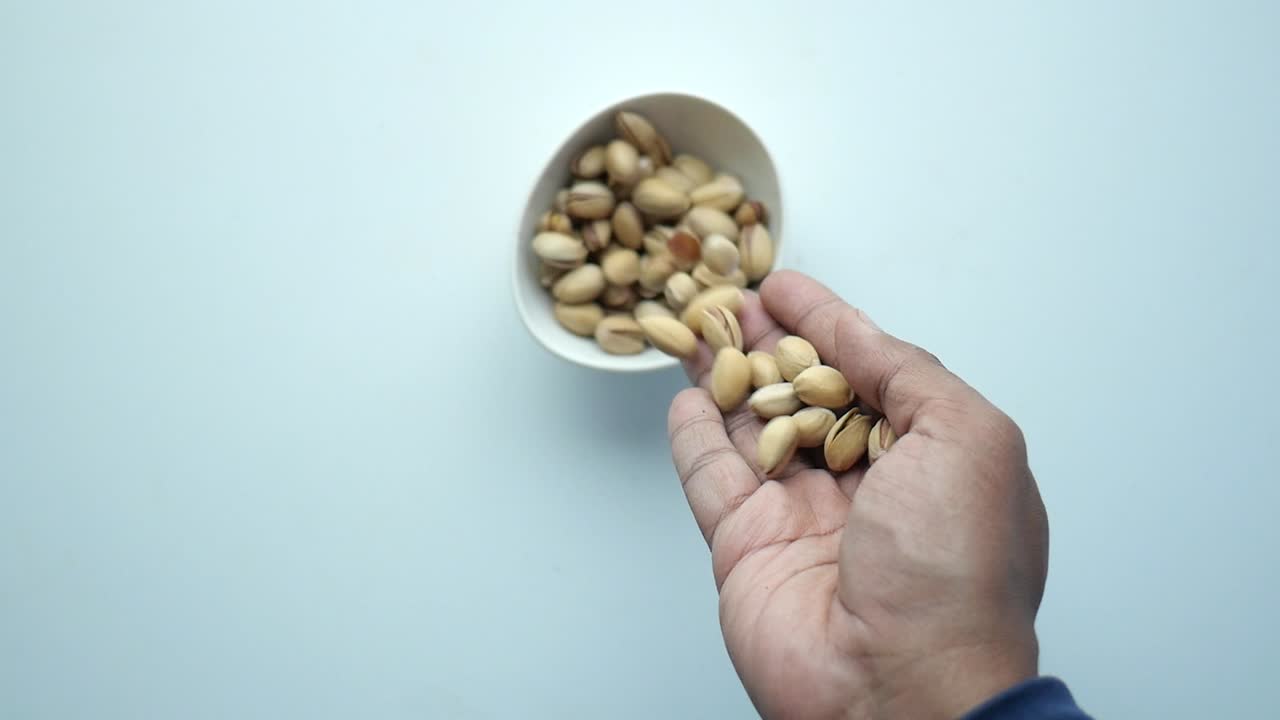 recogiendo con la mano los pistachos de un cuenco
