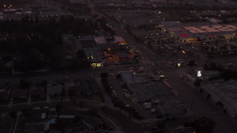 AERIAL:-View-of-Culver-City,-Los-Angeles,-California-traffic,-intersection-at-dusk-with-car-traffic-passing-and-parking-lot