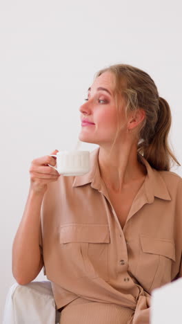 young woman in beige shirt enjoys cup of hot drink and smiles putting hand on closed laptop at office table after working day slow motion