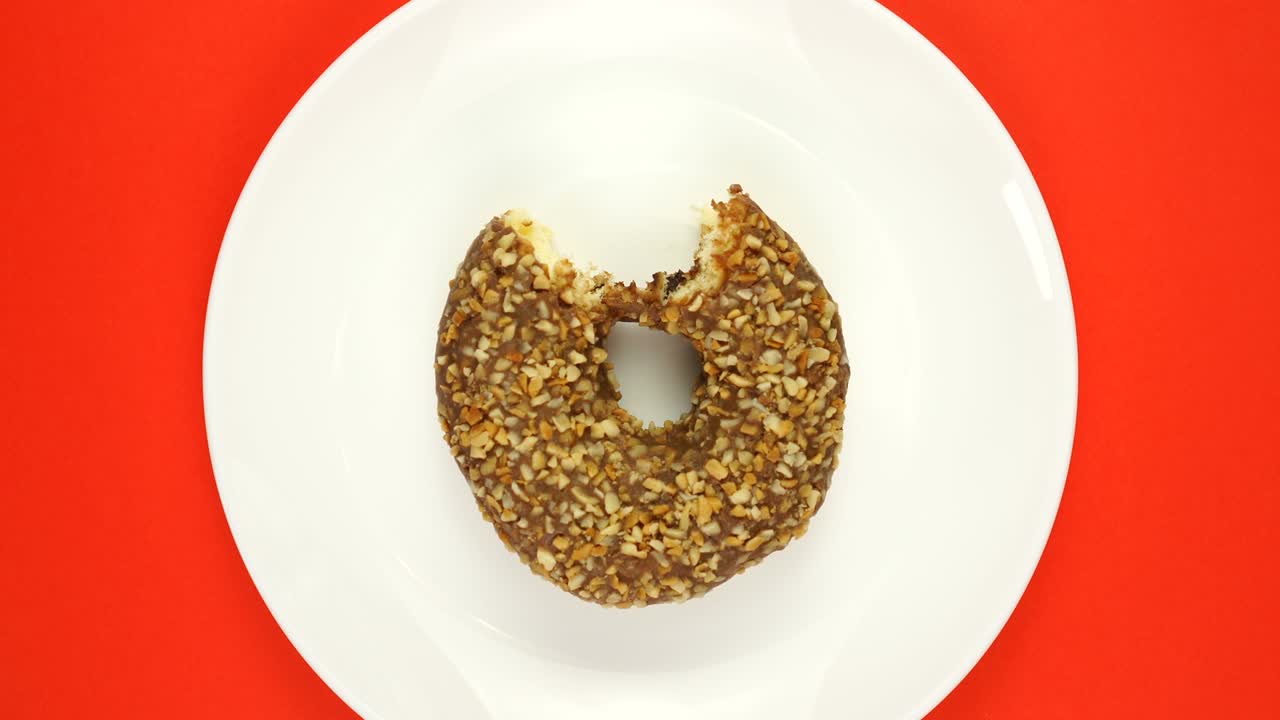 rosquilla fresca cocida con esmaltes multicolores girando sobre un fondo rojo.